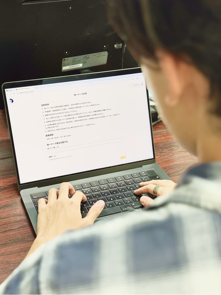 ノートパソコンで統一テーマ案の応募フォームに入力する京大生